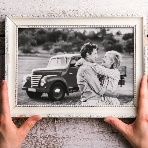 Hands holding picture frame of couple hugging in front of a vintage car