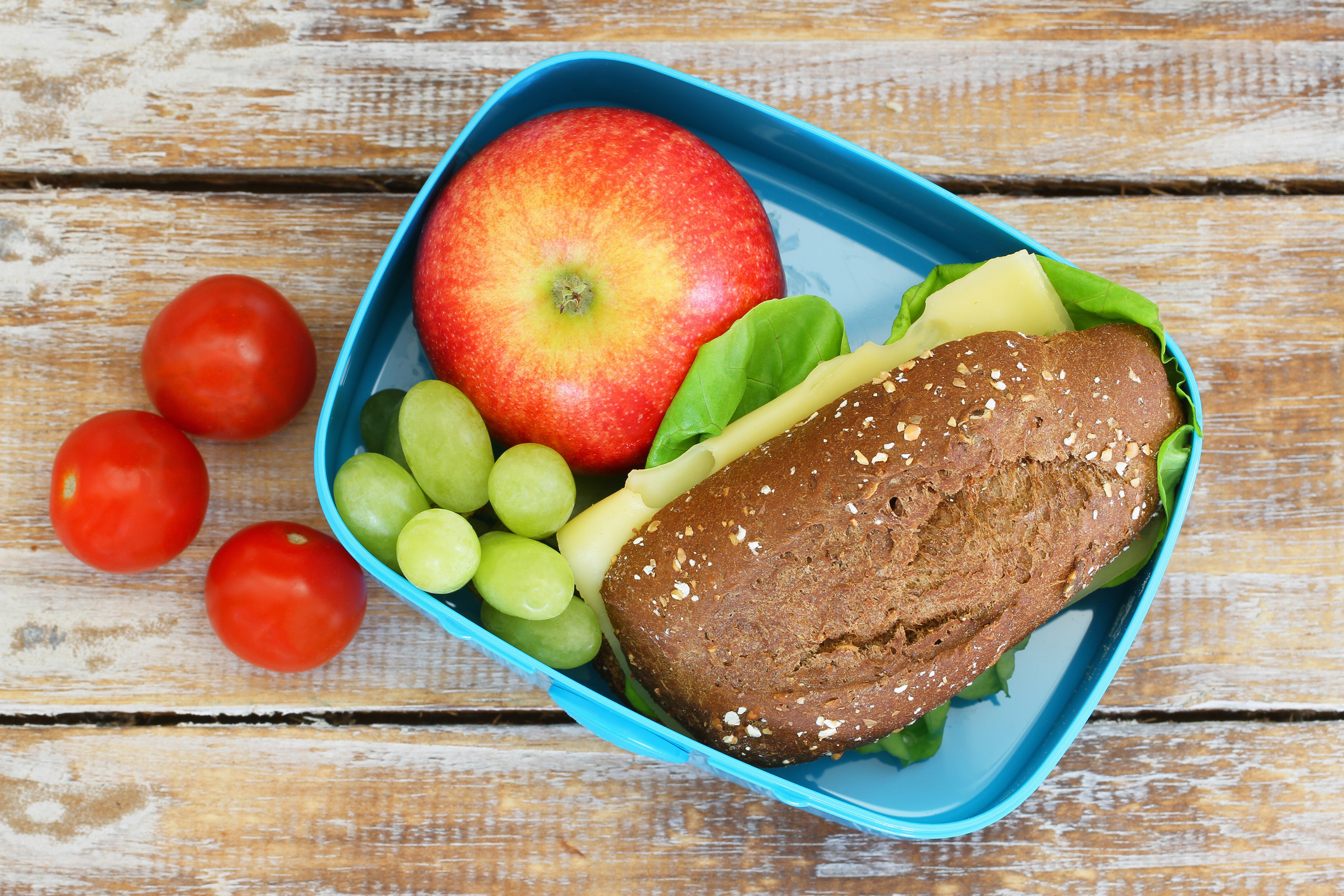Boîte à lunch comprennant un sandwich multi-grain au fromage, une pomme, des raisins, et des tomates cerise